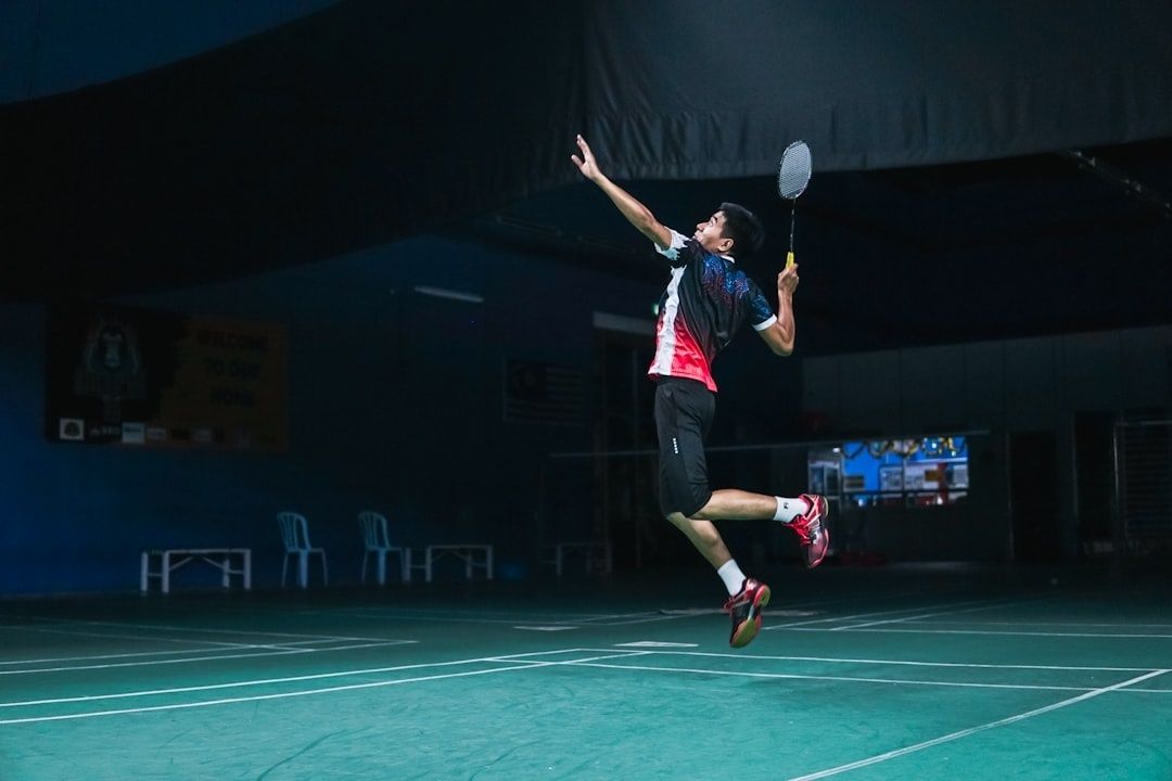 Badmintonspelare hoppar och slår en smash på en upplyst inomhusbana